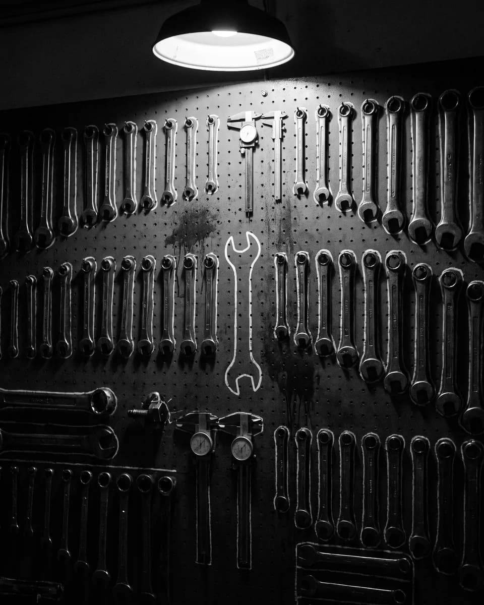 Wrenches hanging in rows on a dark pegboard, one painted outline standing empty under a lamp